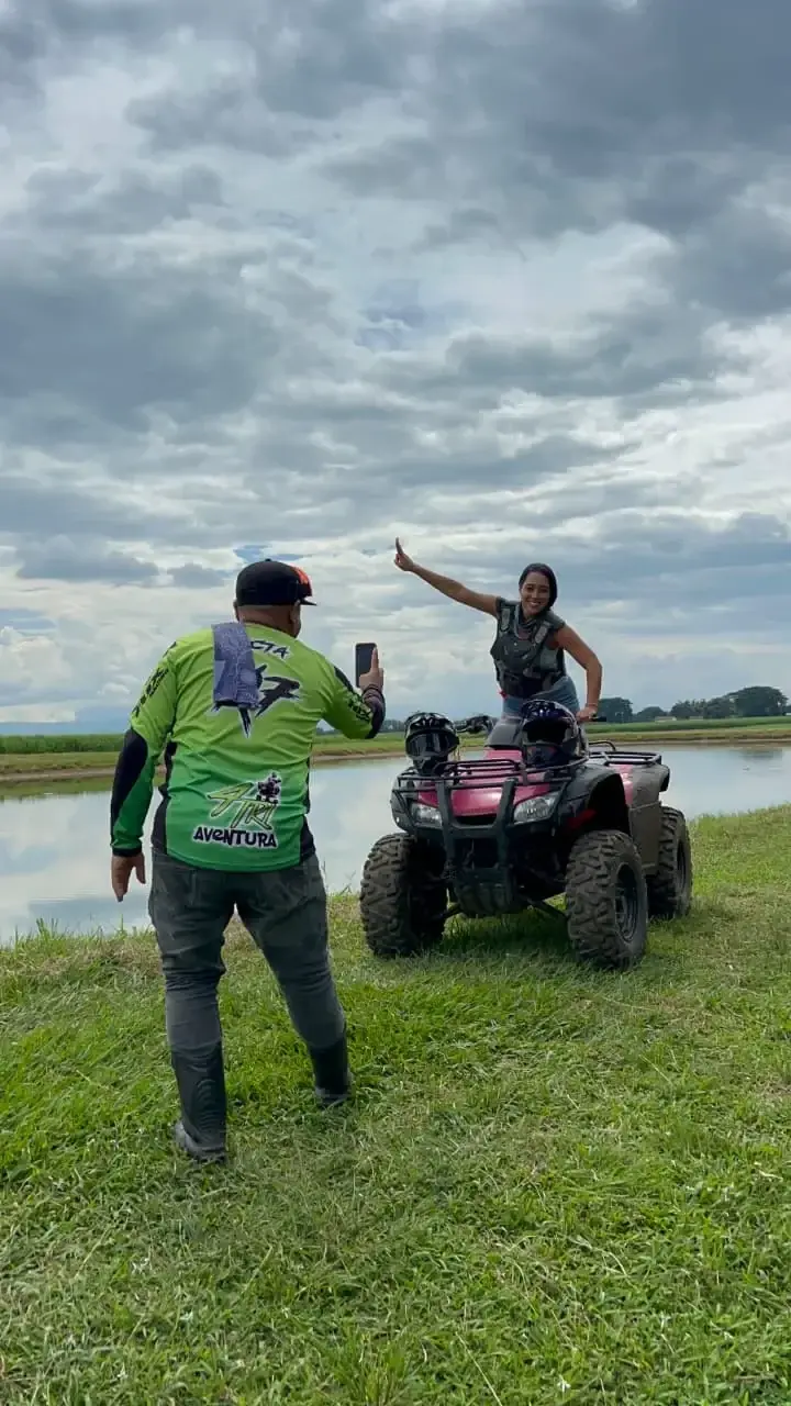 Dos viajeros junto a un lago, uno a punto de subirse a un cuatrimoto, bajo un cielo nublado.