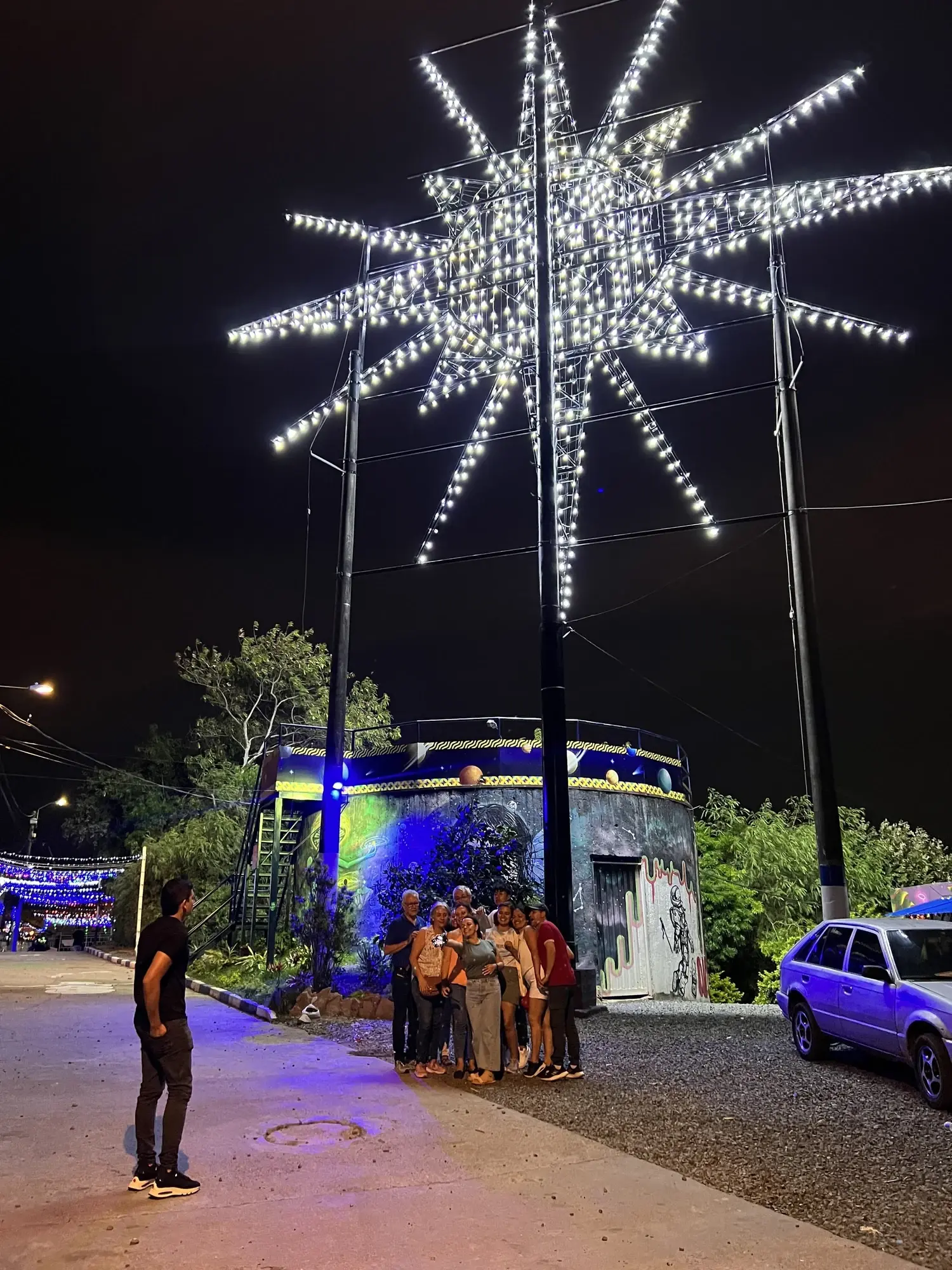 La estrella iluminada del mirador de Siloé, en Cali, de noche, con un pequeño grupo de visitantes debajo.